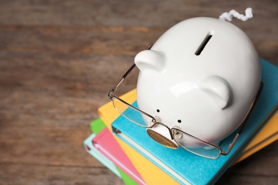 Piggy bank with glasses and books on wooden table. Space for text