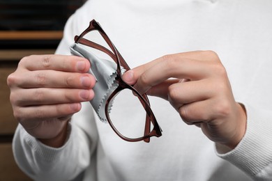 Photo of Man wiping glasses with microfiber cloth indoors, closeup