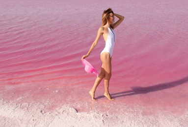 Beautiful woman in swimsuit posing near pink lake on sunny day