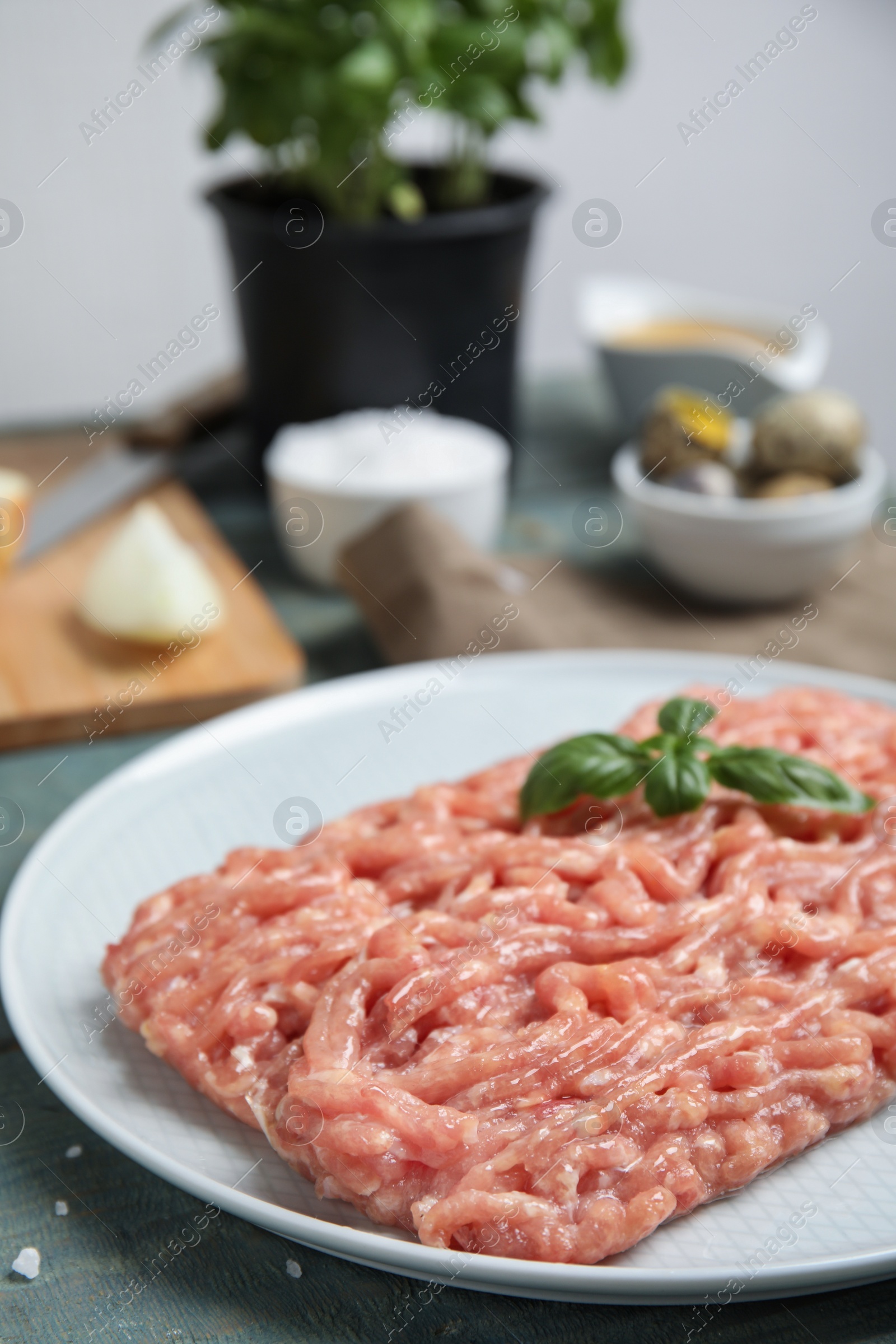 Photo of Raw chicken minced meat with basil on light blue table, closeup