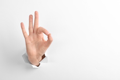 Photo of Woman showing okay sign through hole in torn white paper, closeup. Space for text