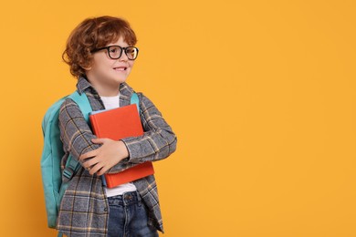 Happy schoolboy with backpack and books on orange background, space for text