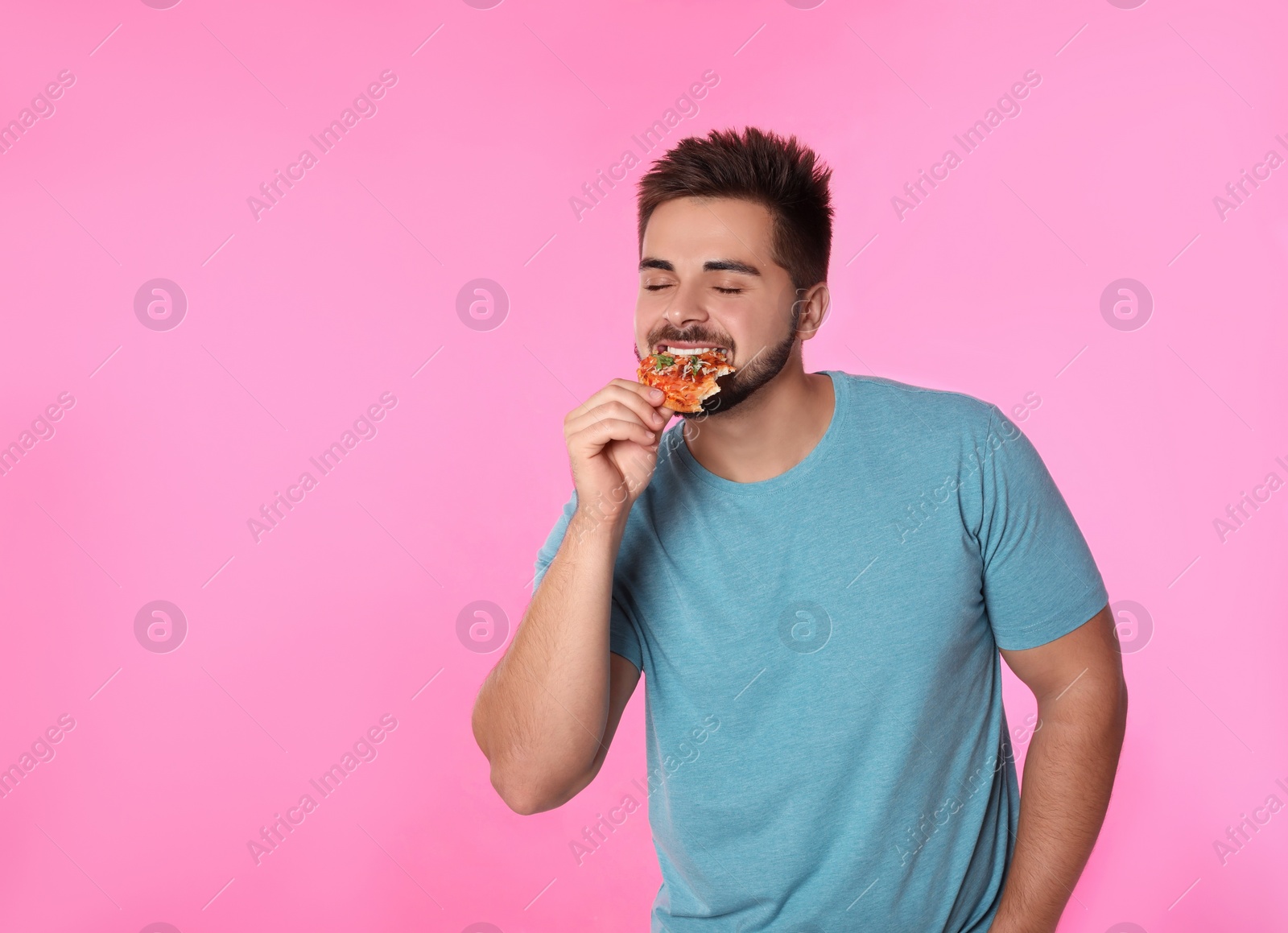 Photo of Handsome man eating pizza on pink background, space for text
