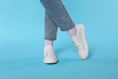 Photo of Woman wearing stylish white sneakers on light blue background, closeup