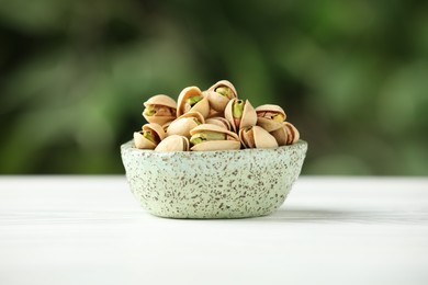 Tasty pistachios in bowl on white table against blurred background