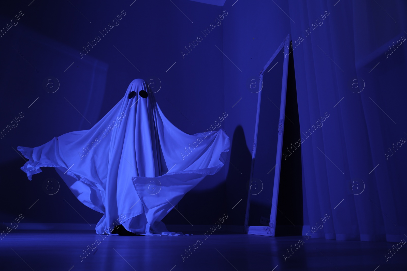 Photo of Creepy ghost. Woman covered with sheet in blue light, low angle view