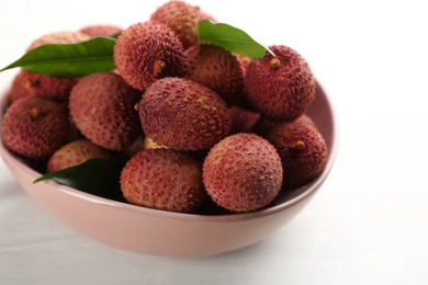 Photo of Fresh ripe lychees in bowl on white wooden table, closeup