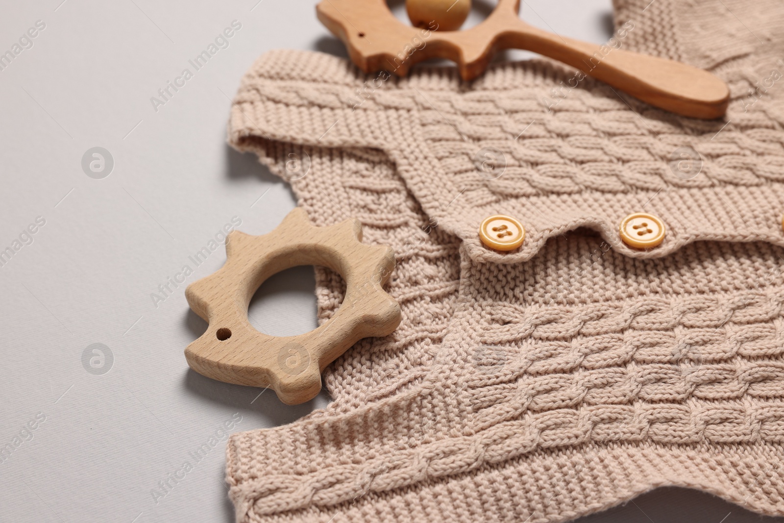 Photo of Baby accessories. Wooden rattle, teether and knitted cloth on grey background, closeup