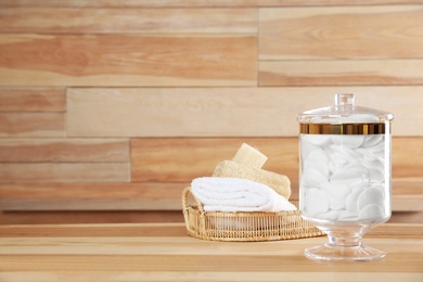 Photo of Decorative glass jar with cotton pads and bathroom accessories on table against wooden background. Space for text