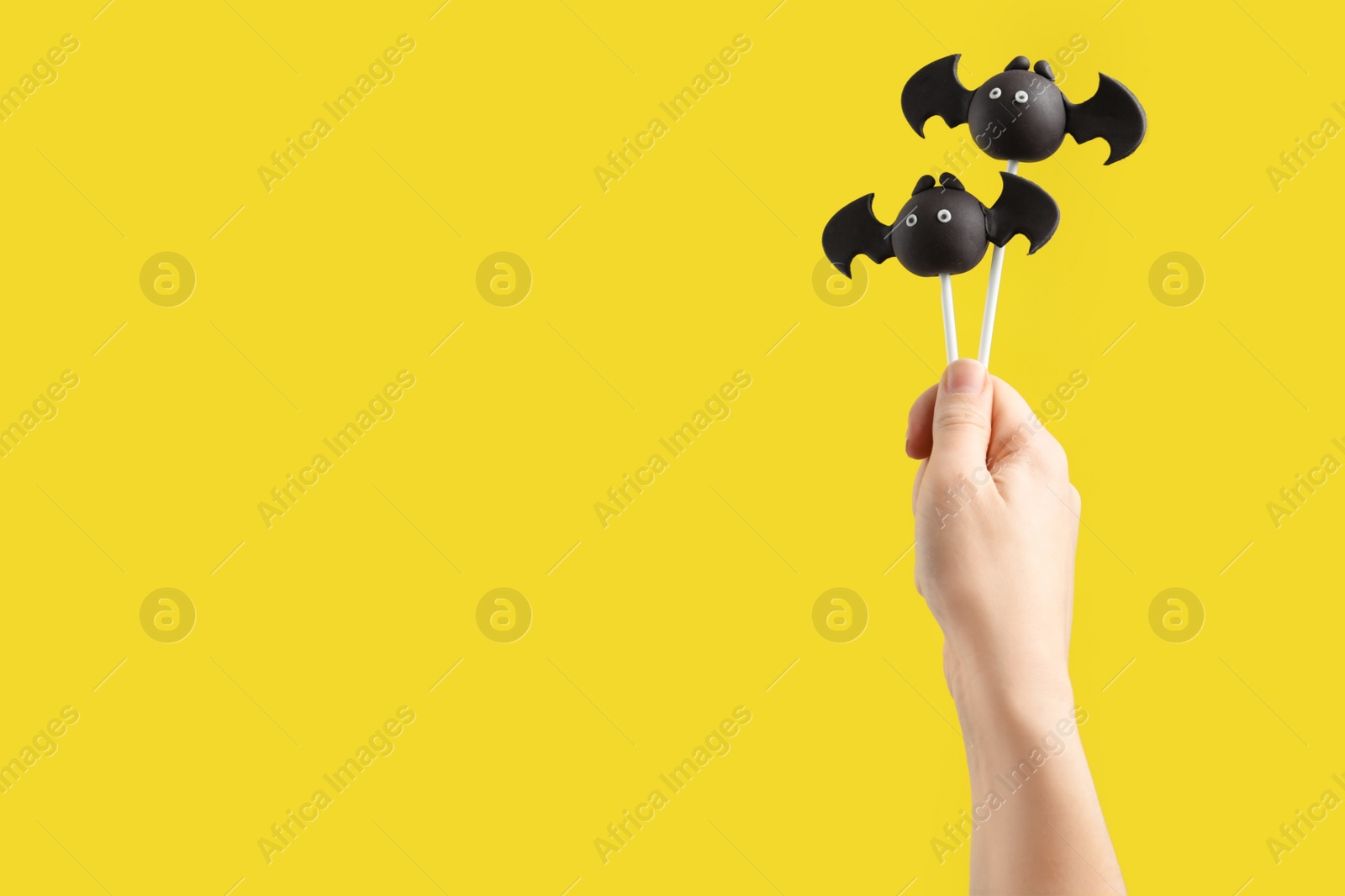Photo of Woman with delicious bat shaped cake pops and space for text on yellow background, closeup. Halloween celebration