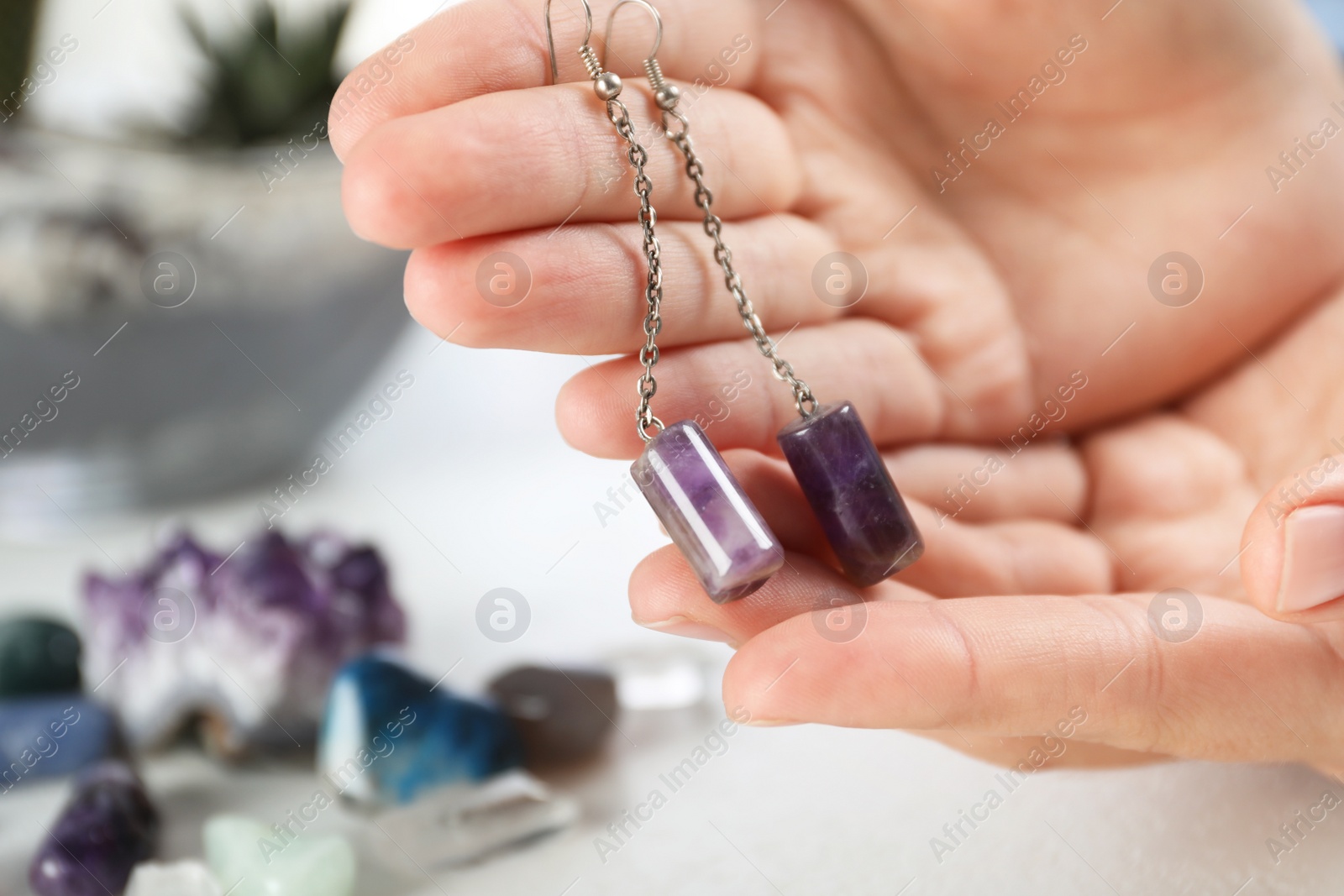 Photo of Woman holding handmade gemstone earrings at table, closeup