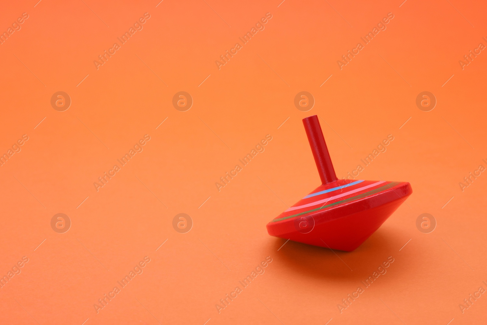 Photo of One bright spinning top on orange background, space for text. Toy whirligig