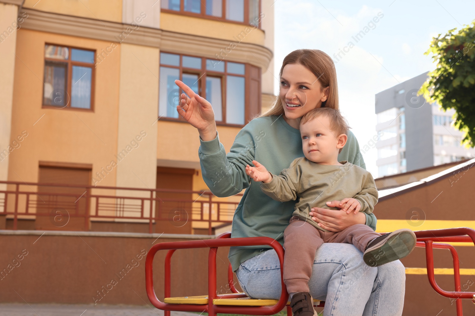 Photo of Happy nanny with cute little boy sitting on carousel outdoors, space for text
