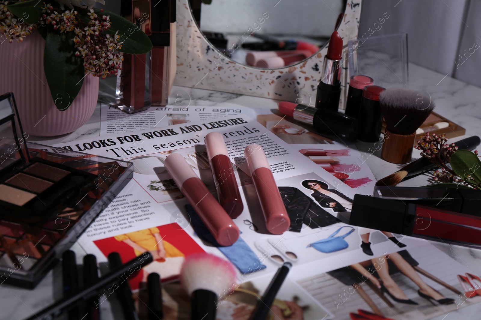 Photo of Bright lip glosses among different cosmetic products and fashion magazine on table indoors