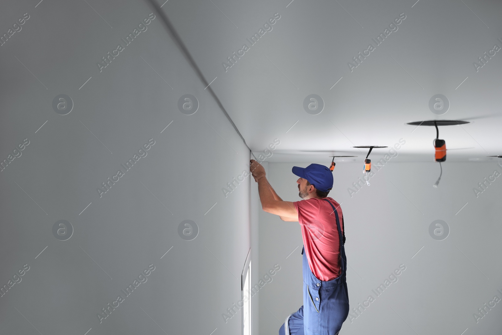 Photo of Worker installing stretch ceiling in empty room