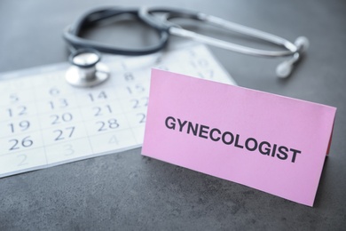 Card with word GYNECOLOGIST near calendar on table