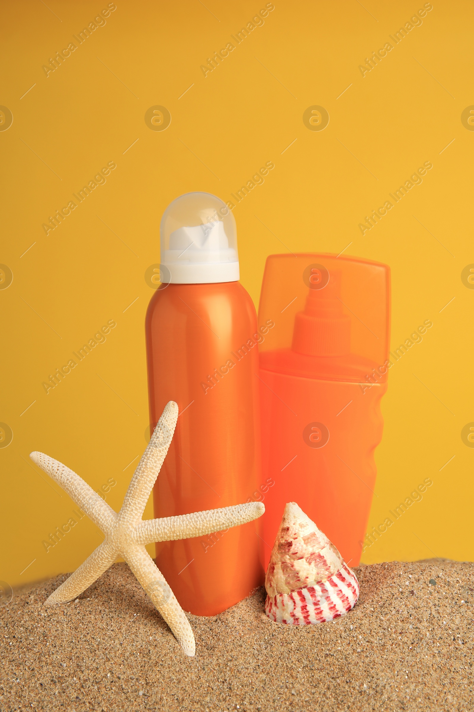 Photo of Sand with bottles of sunscreens, starfish and seashell against orange background. Sun protection