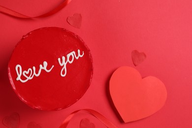 Photo of Bento cake with text Love You, ribbon, paper hearts and space for text on red table, flat lay. St. Valentine's day surprise