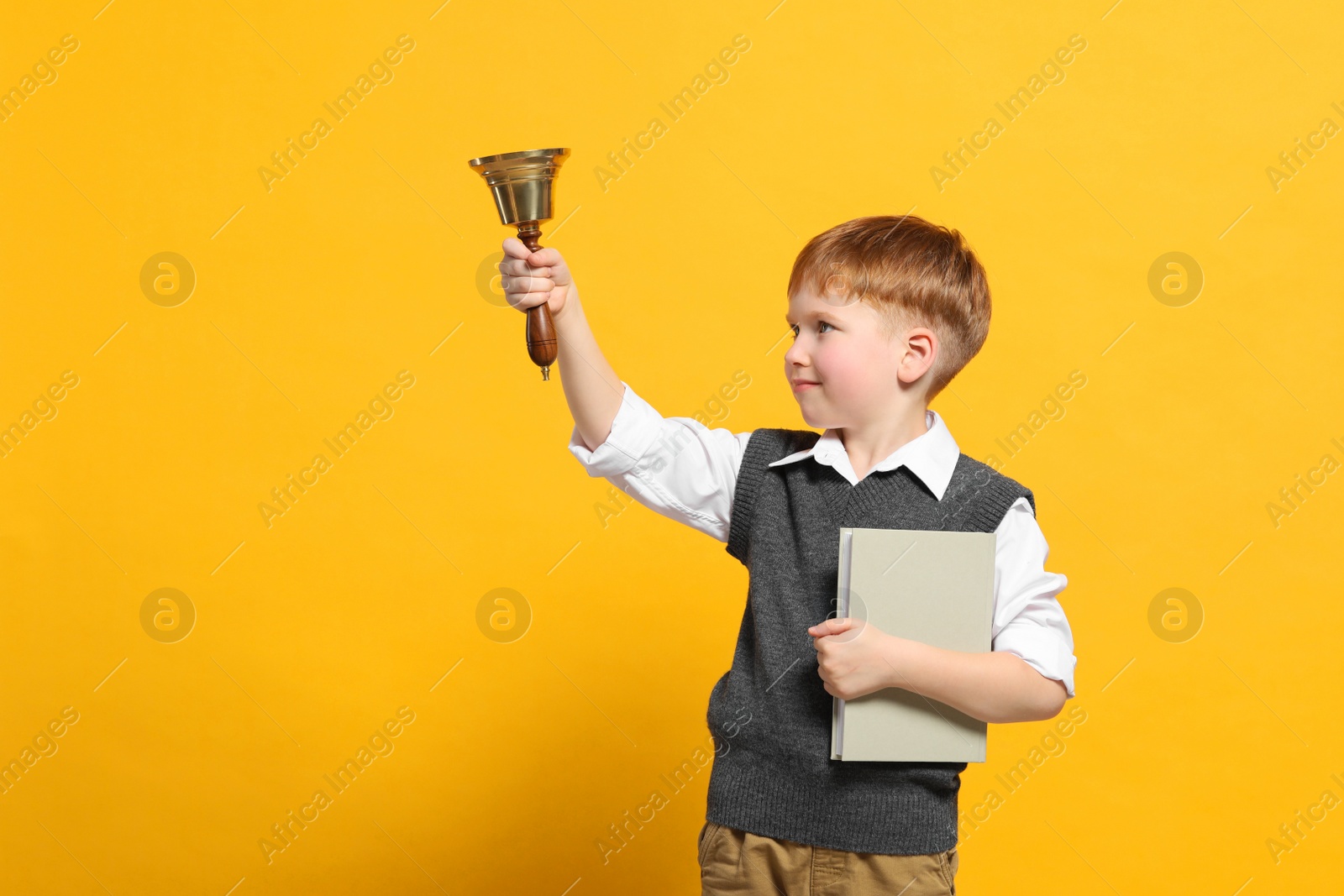 Photo of Pupil with school bell and book on orange background. Space for text