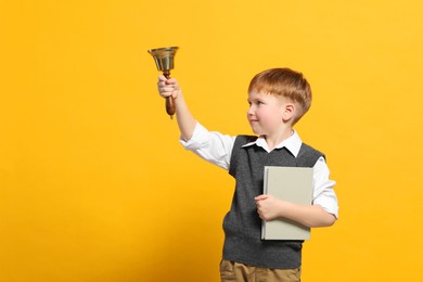 Photo of Pupil with school bell and book on orange background. Space for text