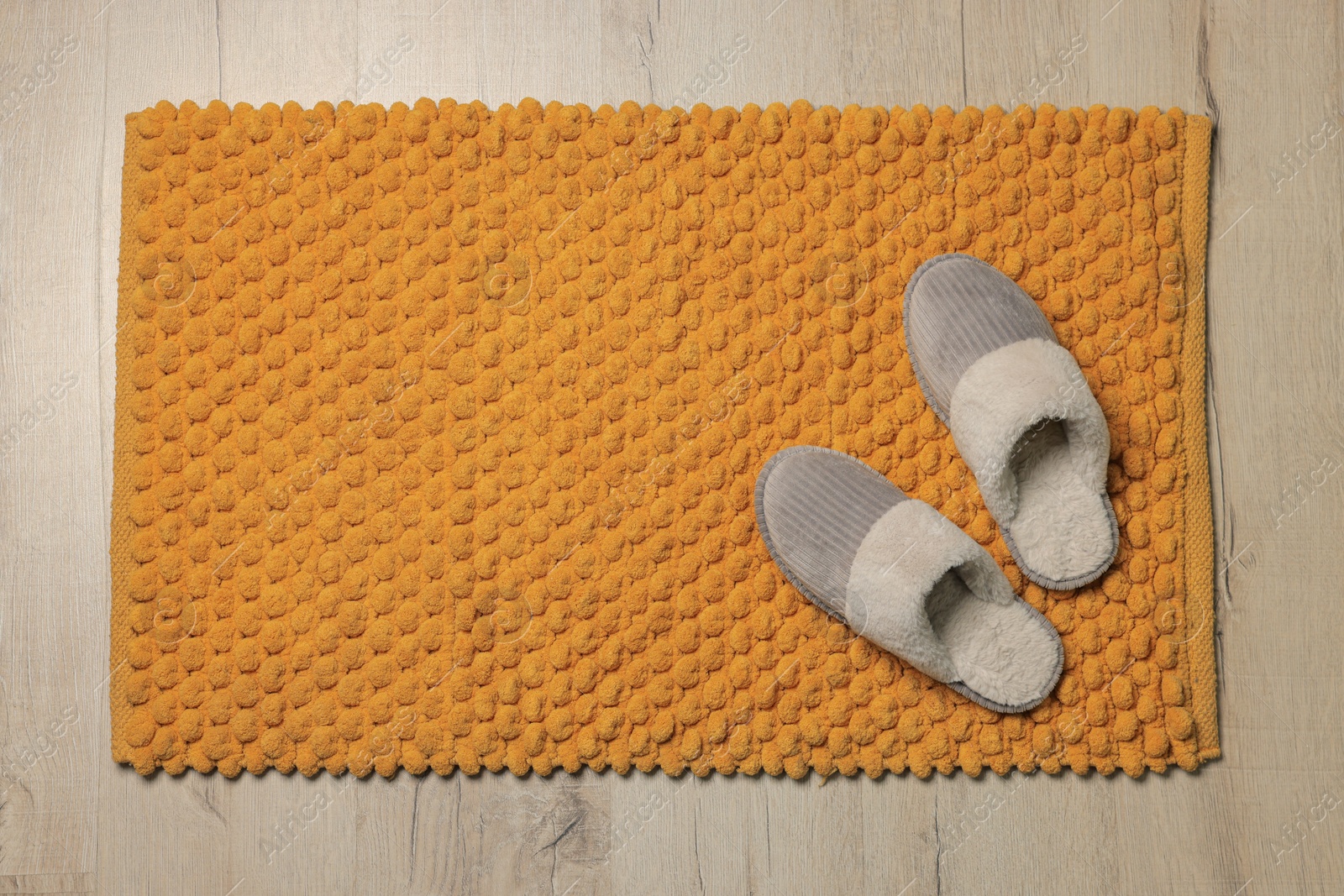 Photo of Soft orange bath mat and slippers on floor, top view