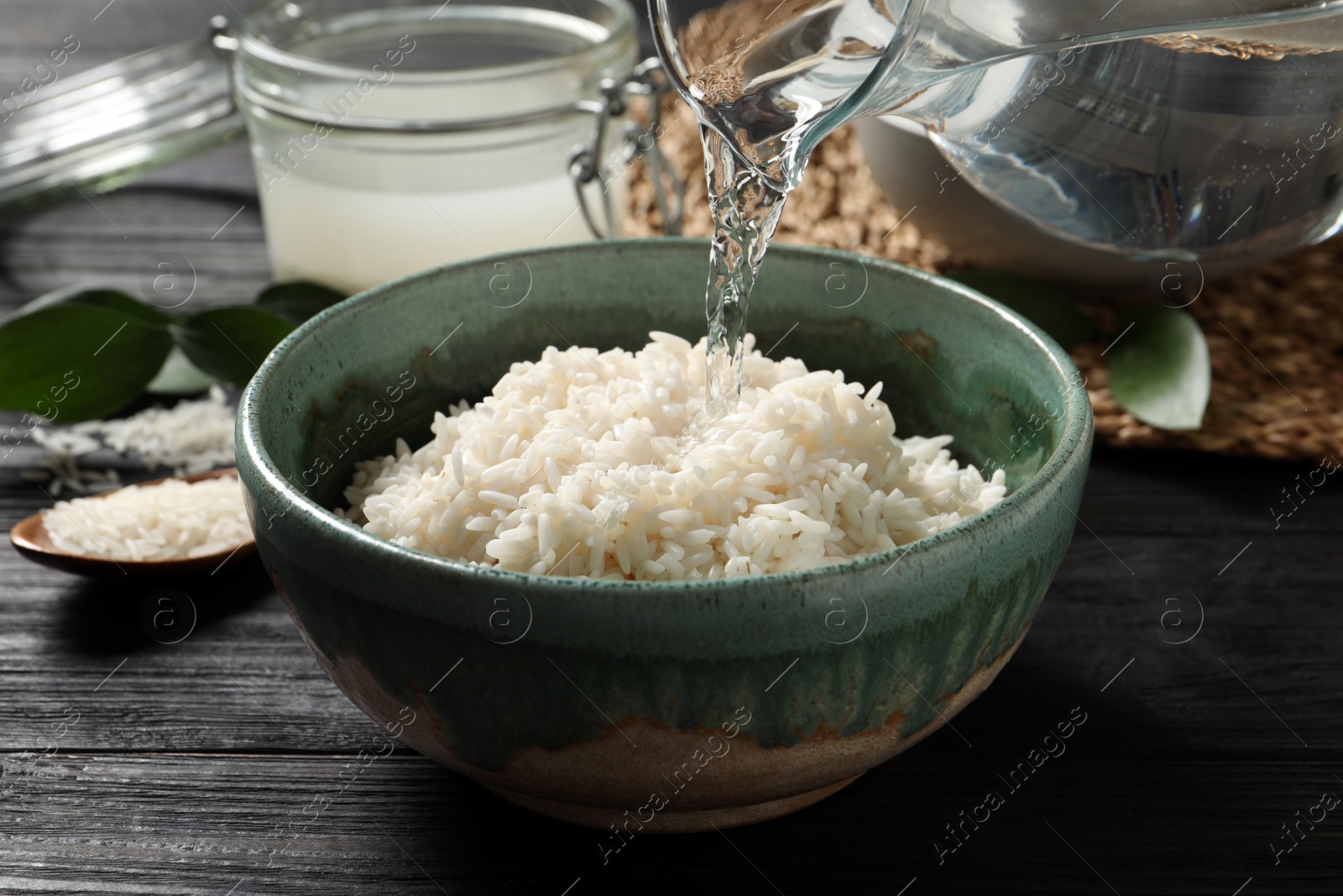 Photo of Pouring water into bowl with rice on wooden table