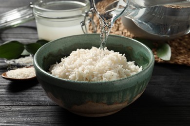 Photo of Pouring water into bowl with rice on wooden table