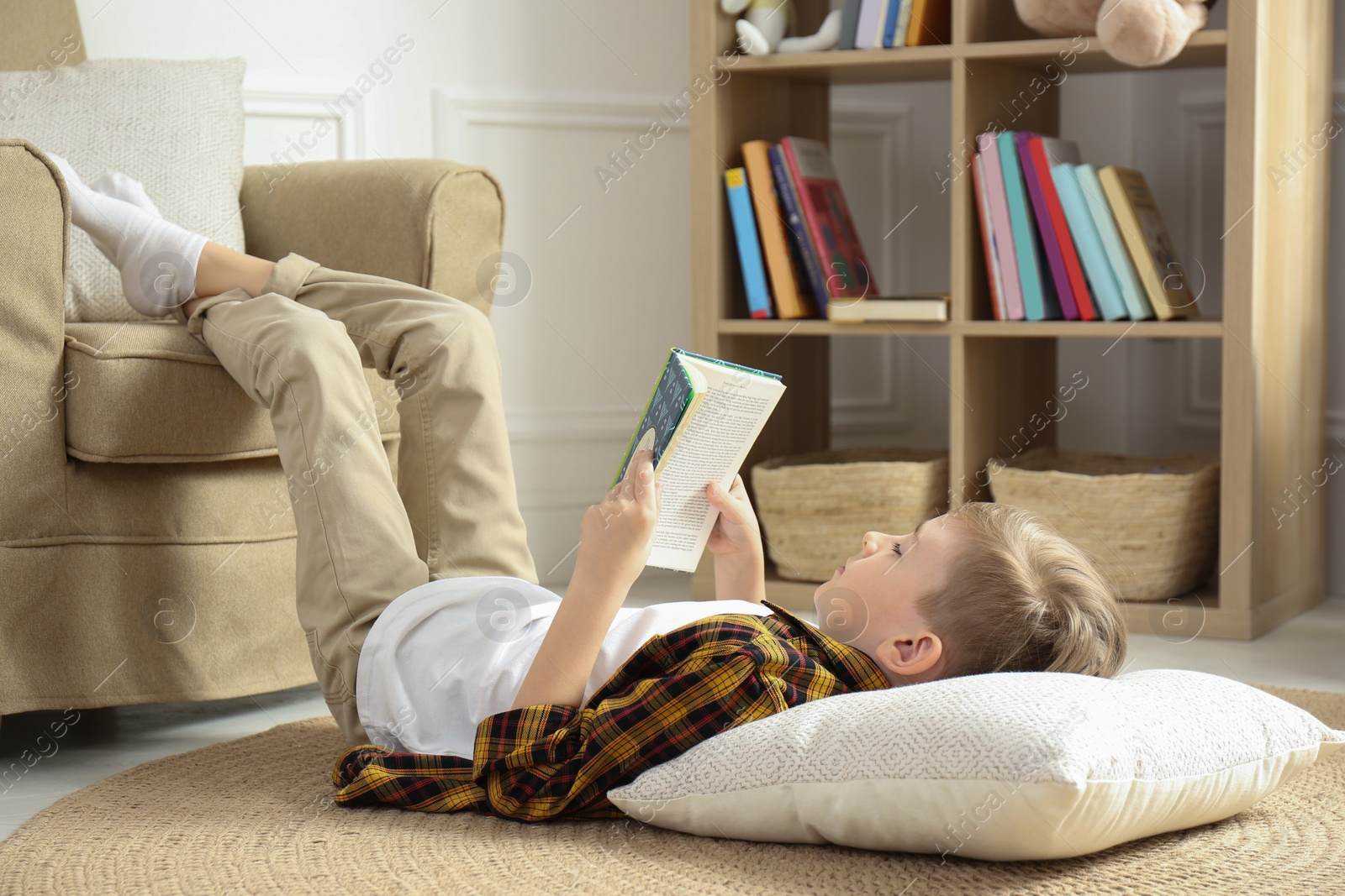 Photo of Little boy reading book on floor at home