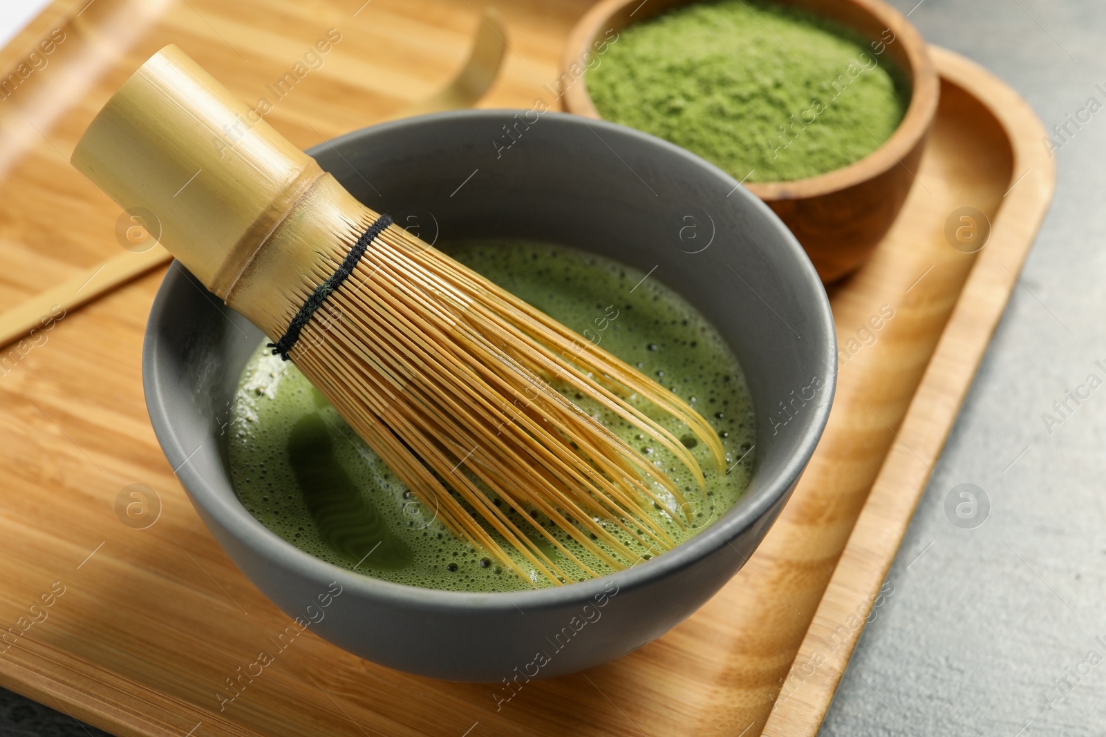 Photo of Cup of fresh matcha tea with bamboo whisk on table, closeup