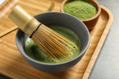 Cup of fresh matcha tea with bamboo whisk on table, closeup