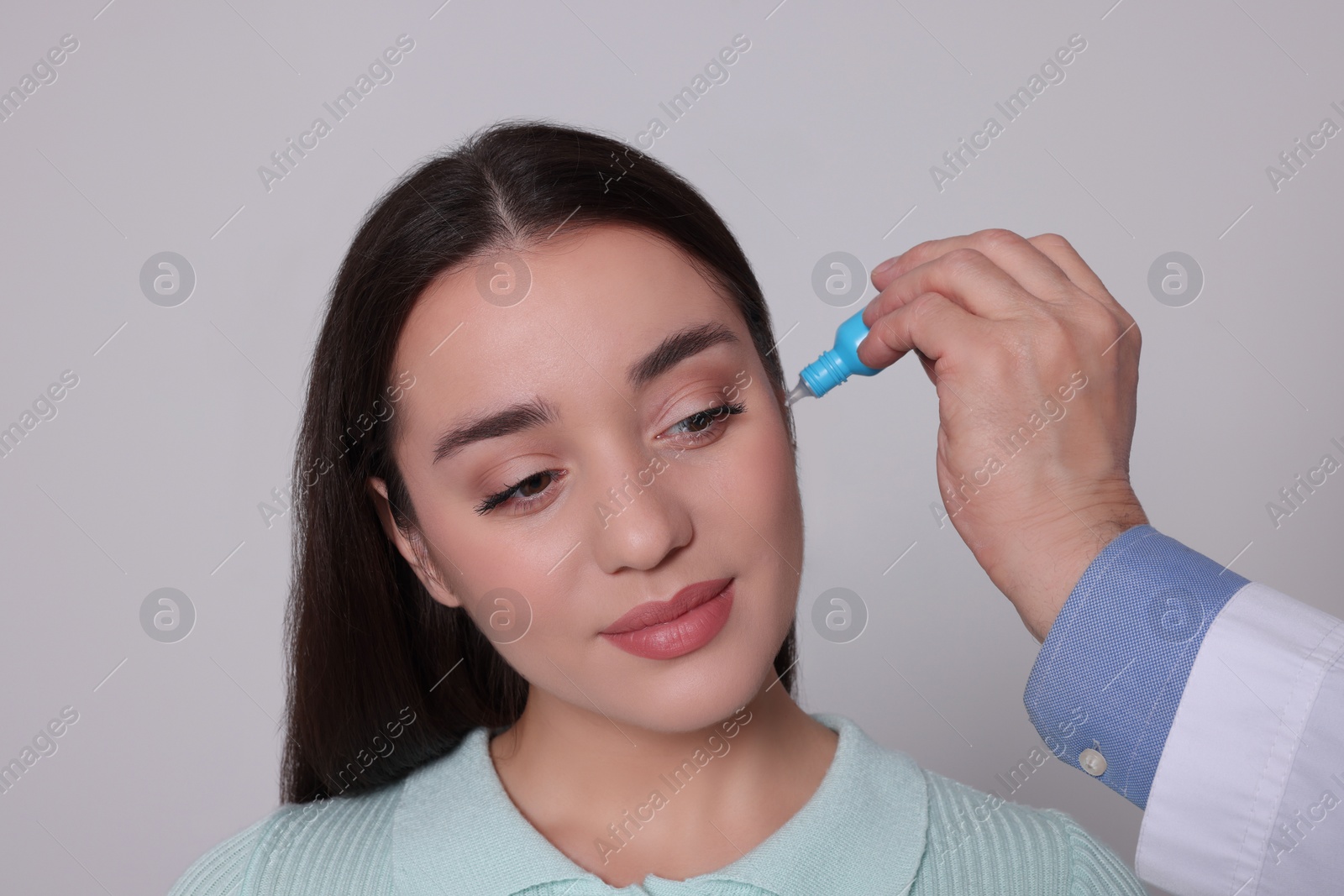 Photo of Doctor dripping medication into woman's ear on light grey background