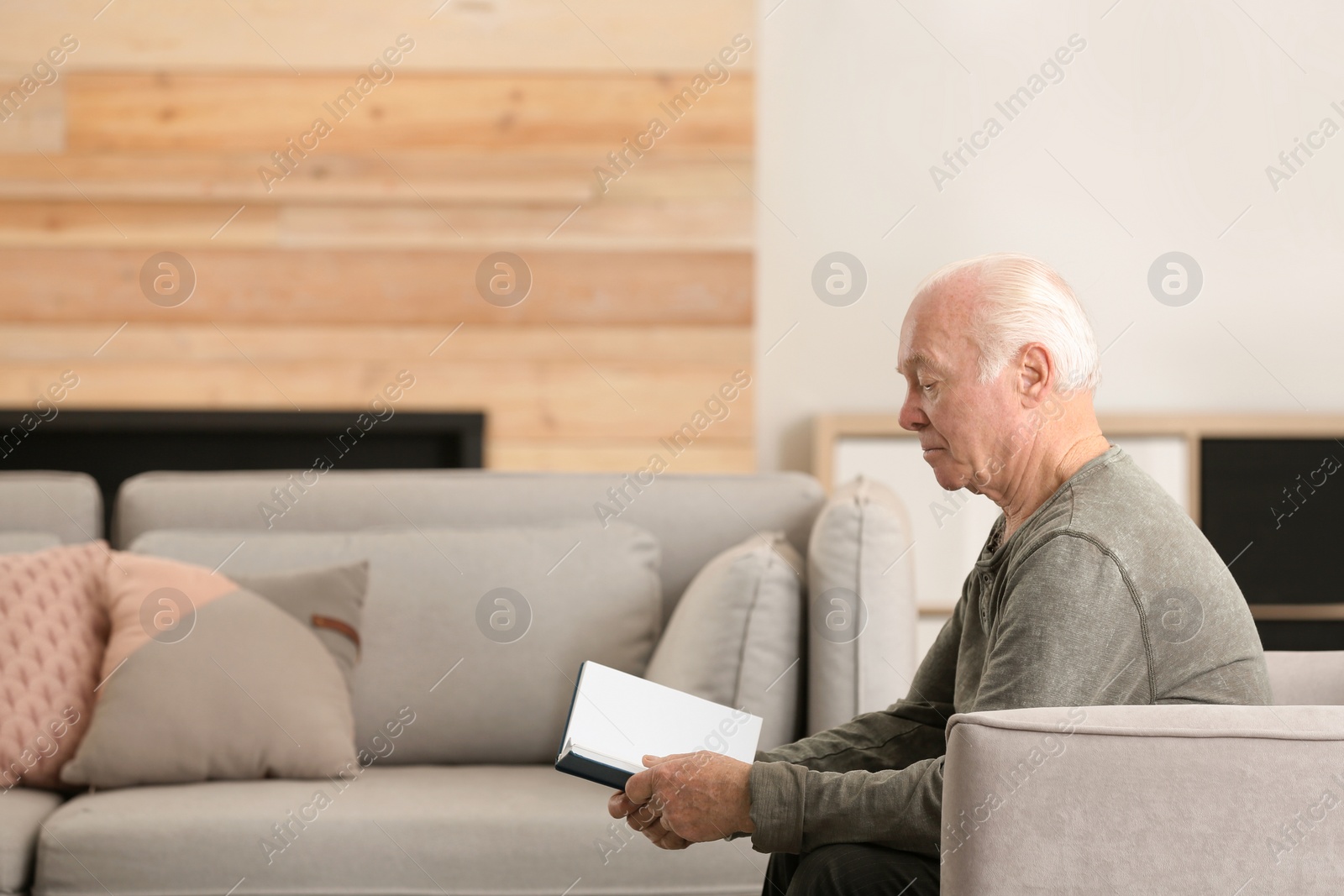 Photo of Elderly man reading book in living room. Space for text