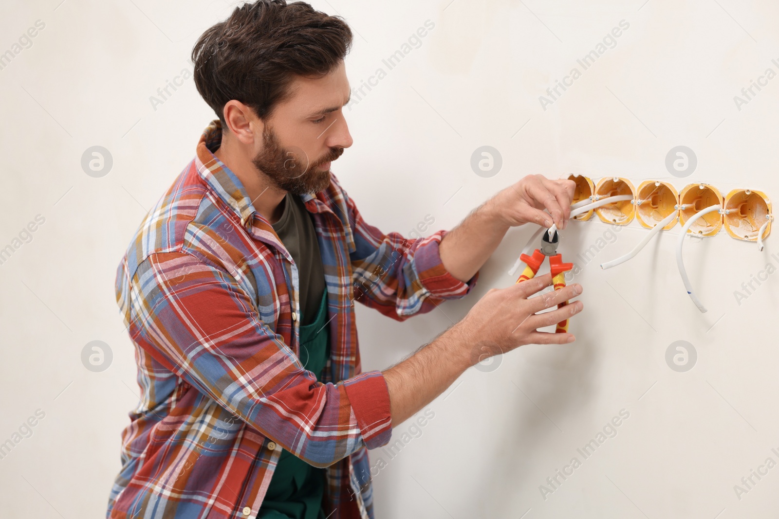 Photo of Professional electrician with pliers fixing wires indoors