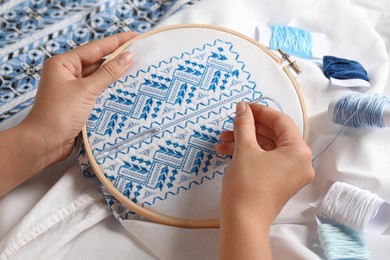Photo of Woman embroidering shirt with blue thread, closeup. Ukrainian national clothes