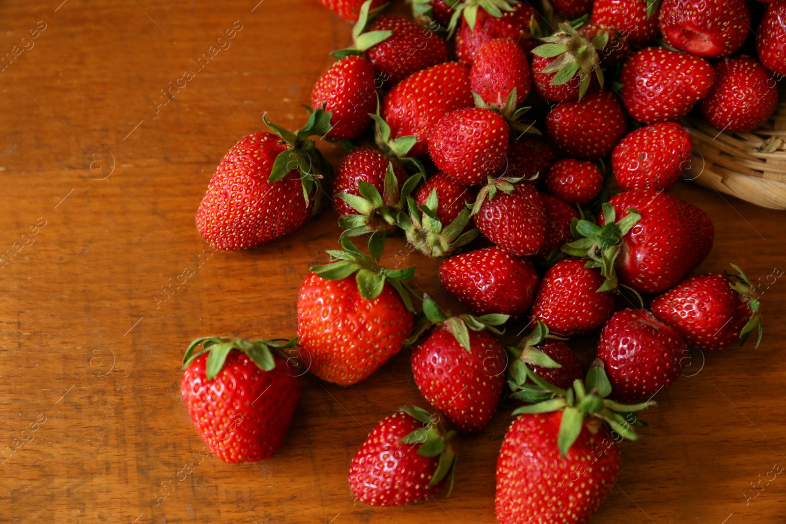 Photo of Basket with scattered ripe strawberries on wooden table, top view