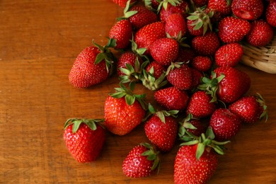 Photo of Basket with scattered ripe strawberries on wooden table, top view