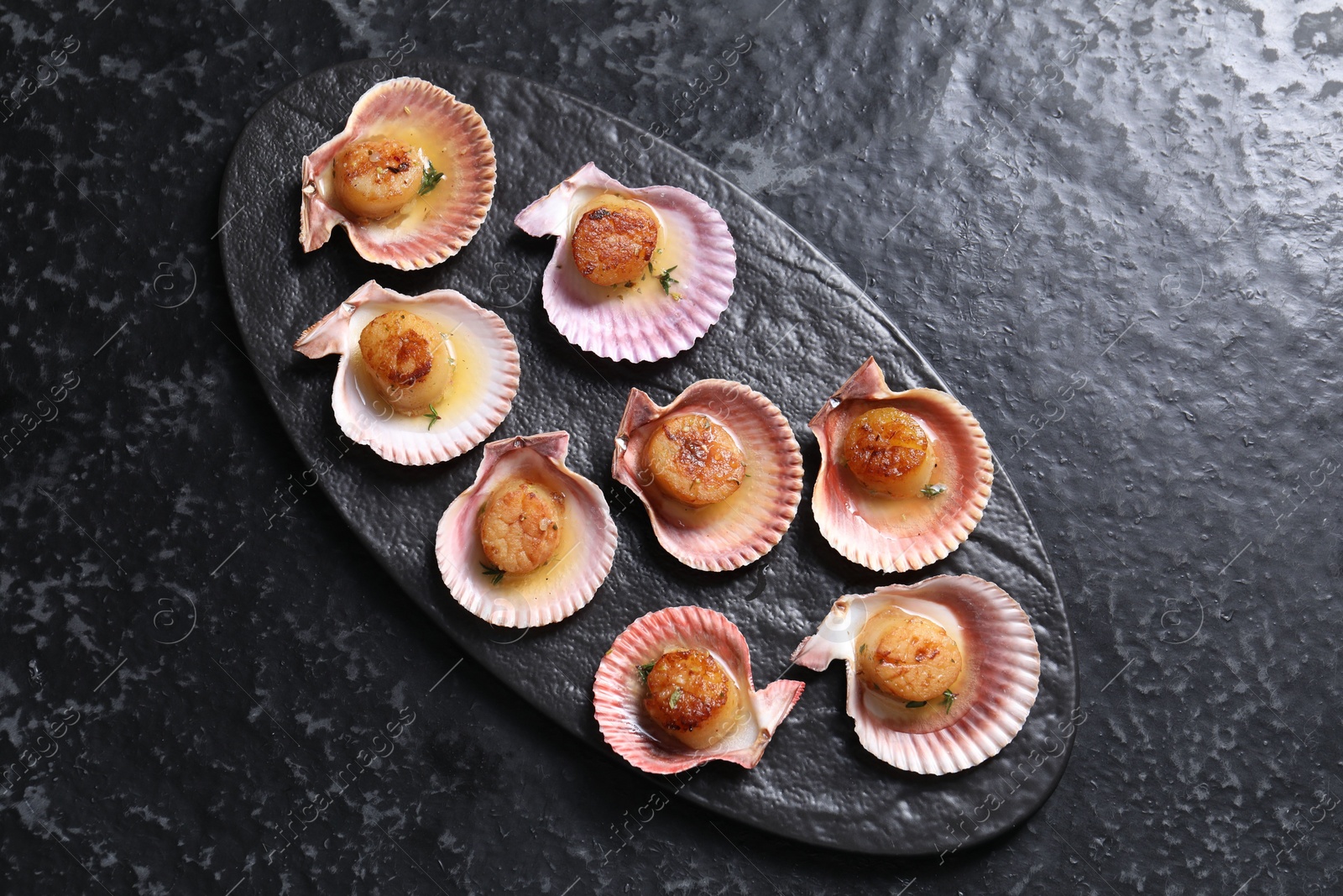 Photo of Delicious fried scallops in shells on black table, top view