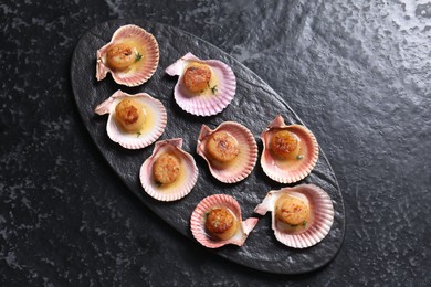 Delicious fried scallops in shells on black table, top view