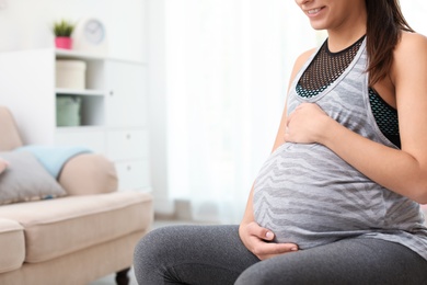 Photo of Young pregnant woman in fitness clothes at home, closeup. Space for text