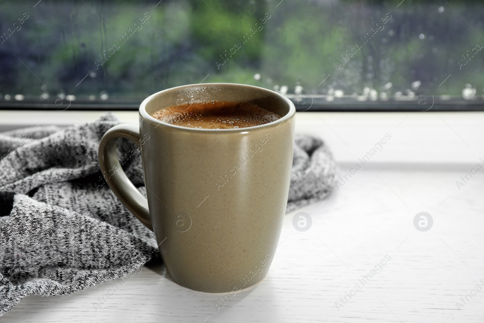 Photo of Cup of hot drink on window sill against glass with rain drops, space for text