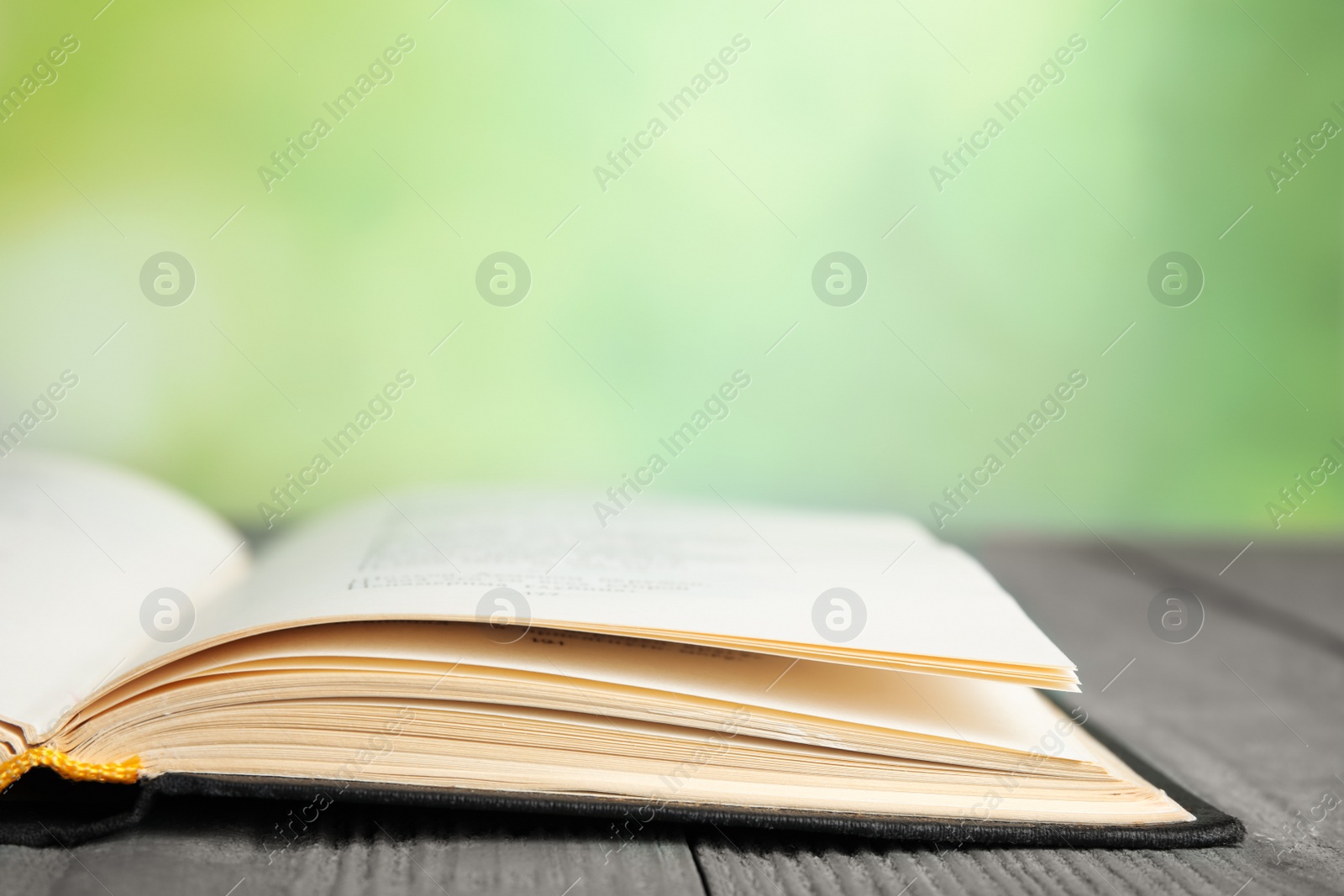 Photo of Open book on blue wooden table against blurred green background, closeup. Space for text