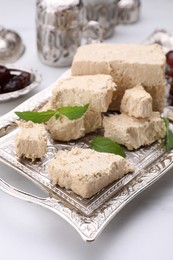 Photo of Pieces of tasty halva, dates and mint leaves on white marble table, closeup