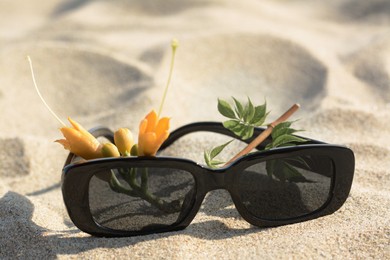 Stylish sunglasses and tropical flower on sand, closeup