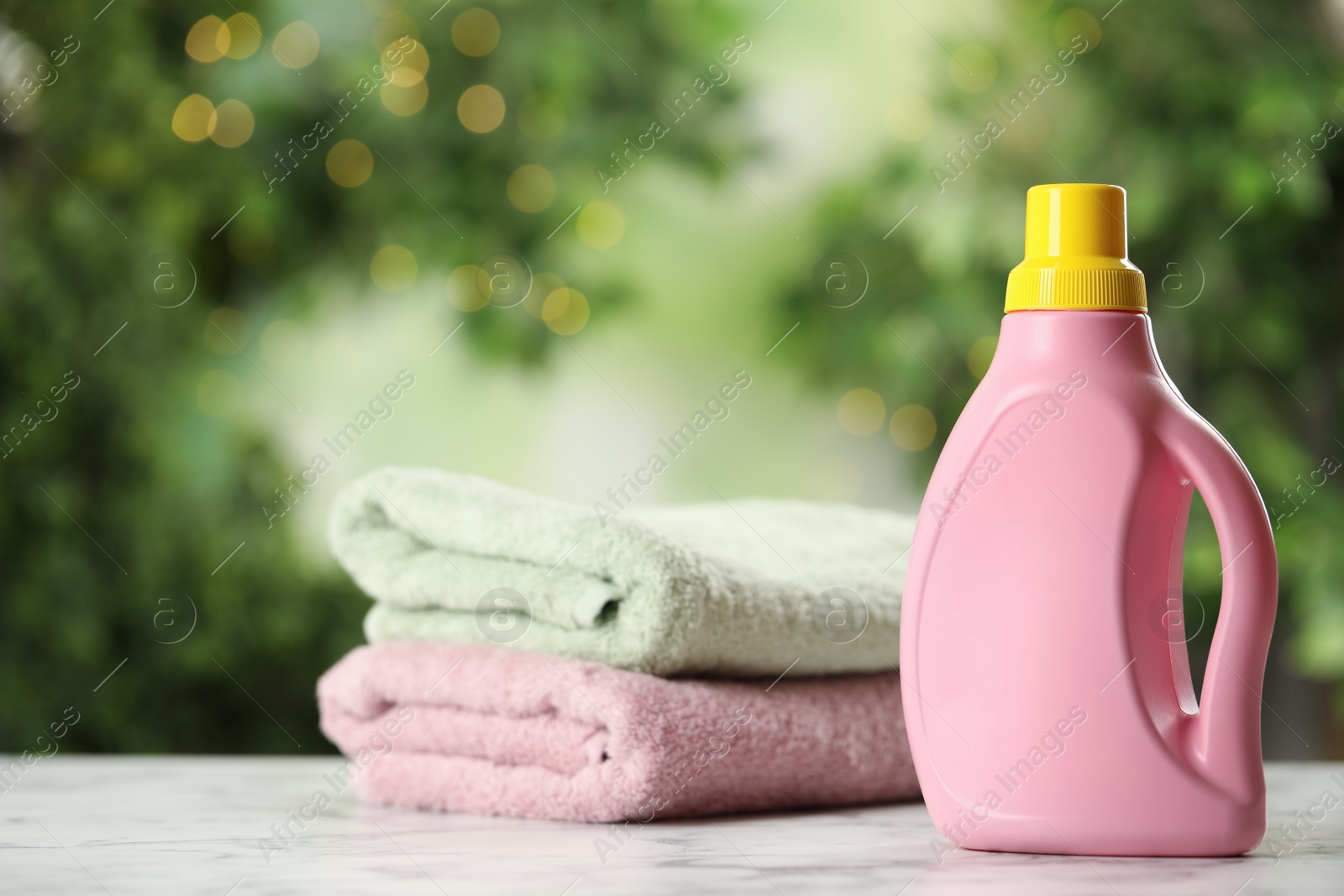 Photo of Stack of fresh towels and detergent on white marble table outdoors