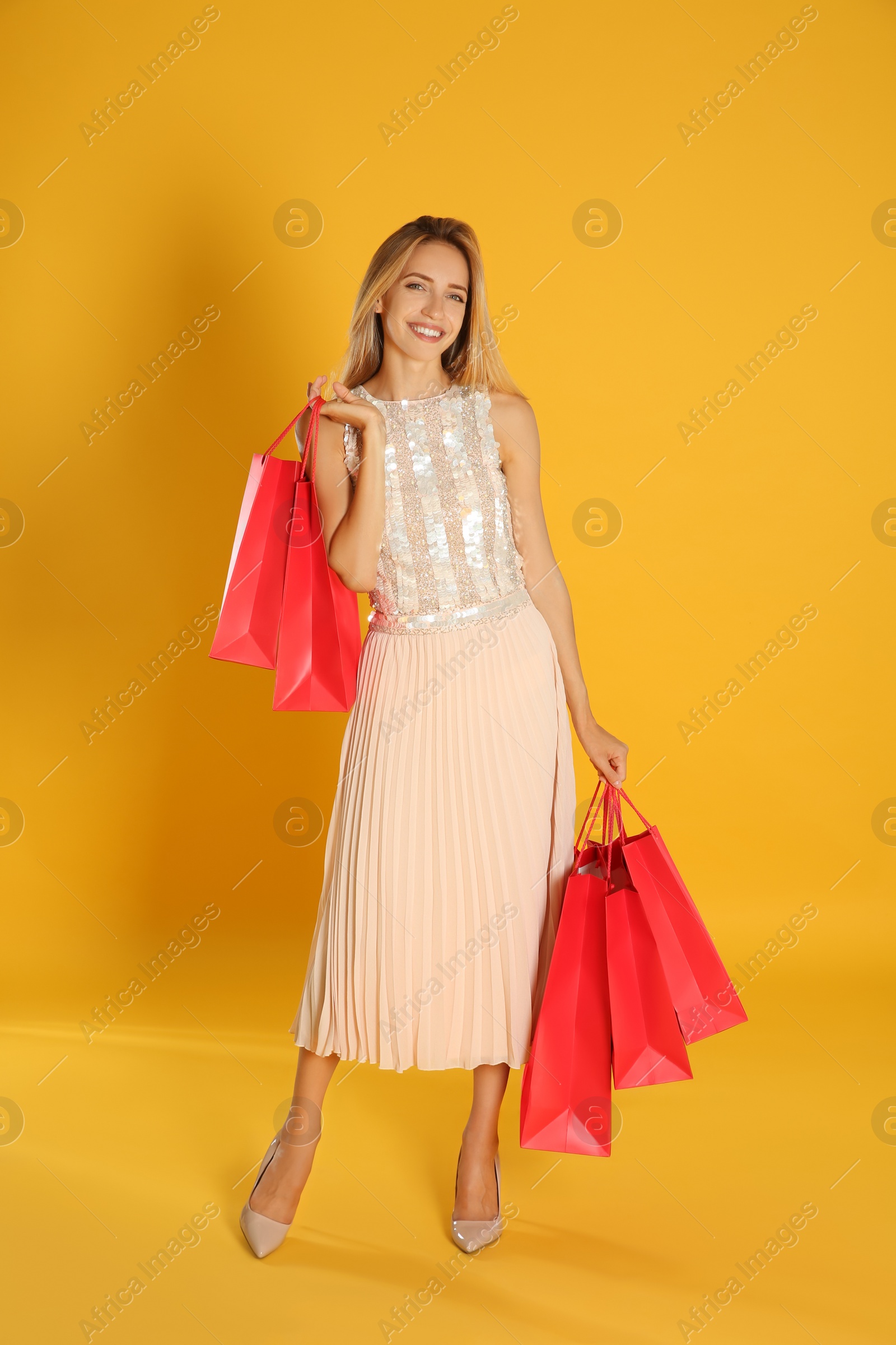 Photo of Happy young woman with shopping bags on yellow background. Black Friday Sale