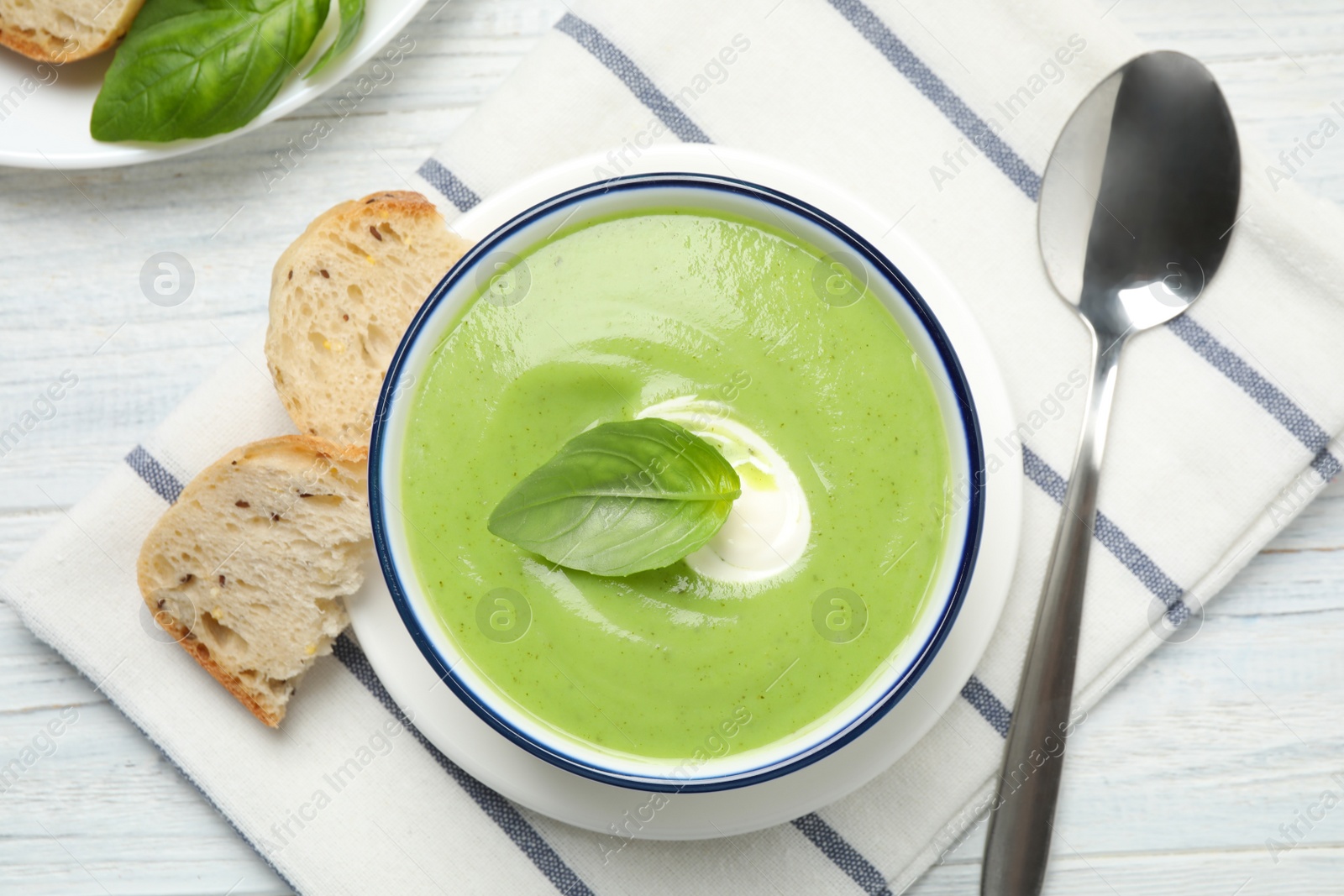 Photo of Tasty homemade zucchini cream soup served on white wooden table, flat lay