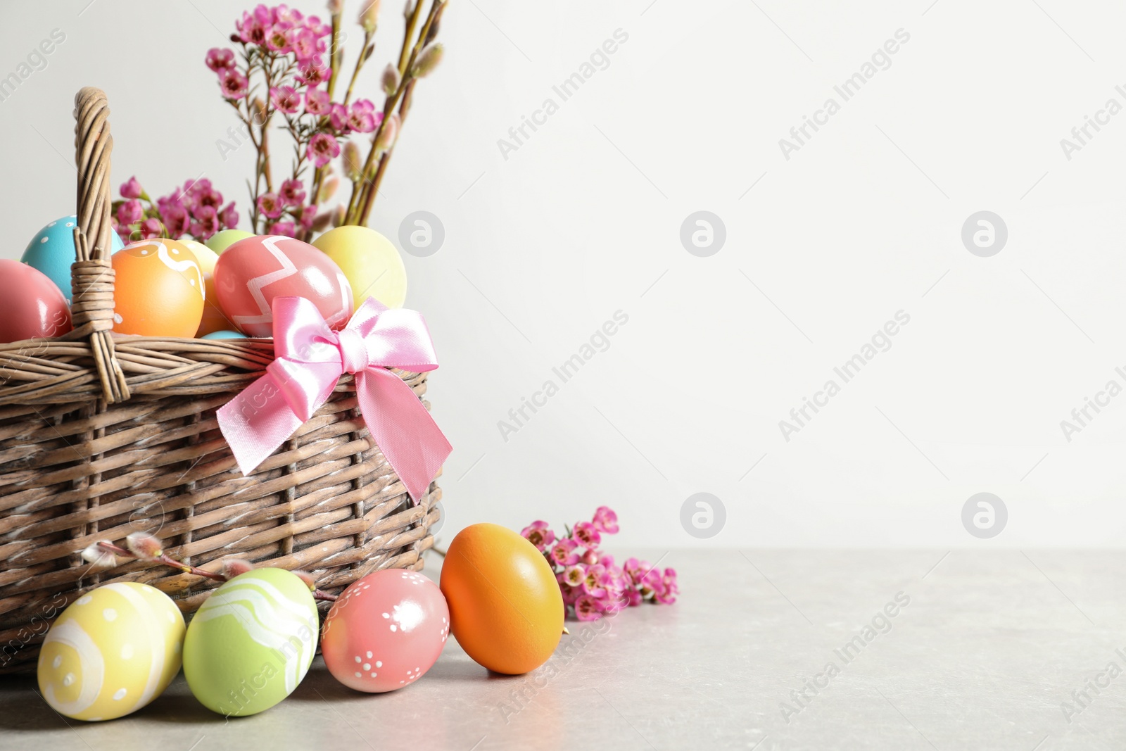 Photo of Wicker basket with painted Easter eggs and flowers on table, space for text