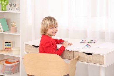 Photo of Little boy drawing at desk in room. Home workplace