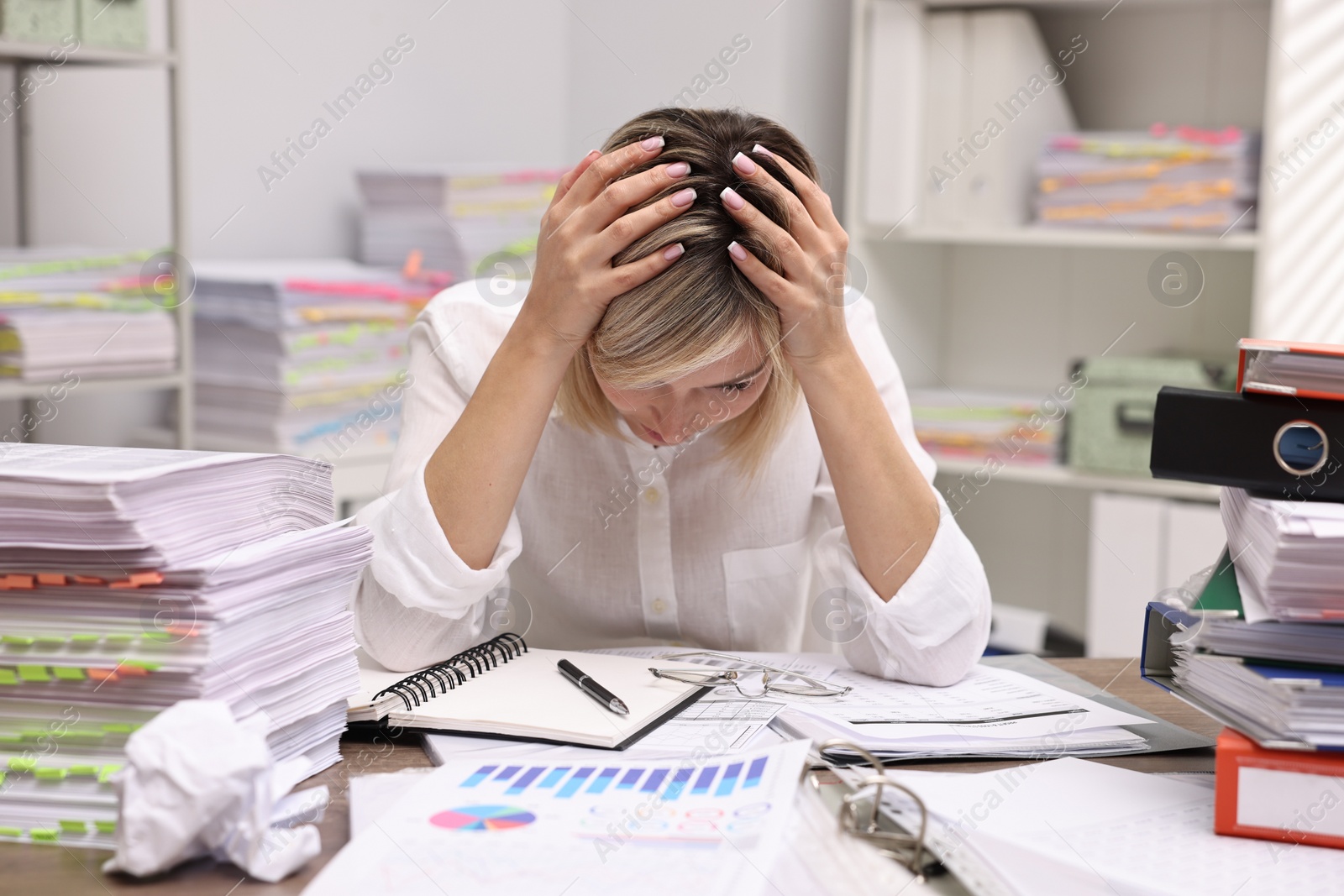 Photo of Overwhelmed woman surrounded by documents at workplace in office