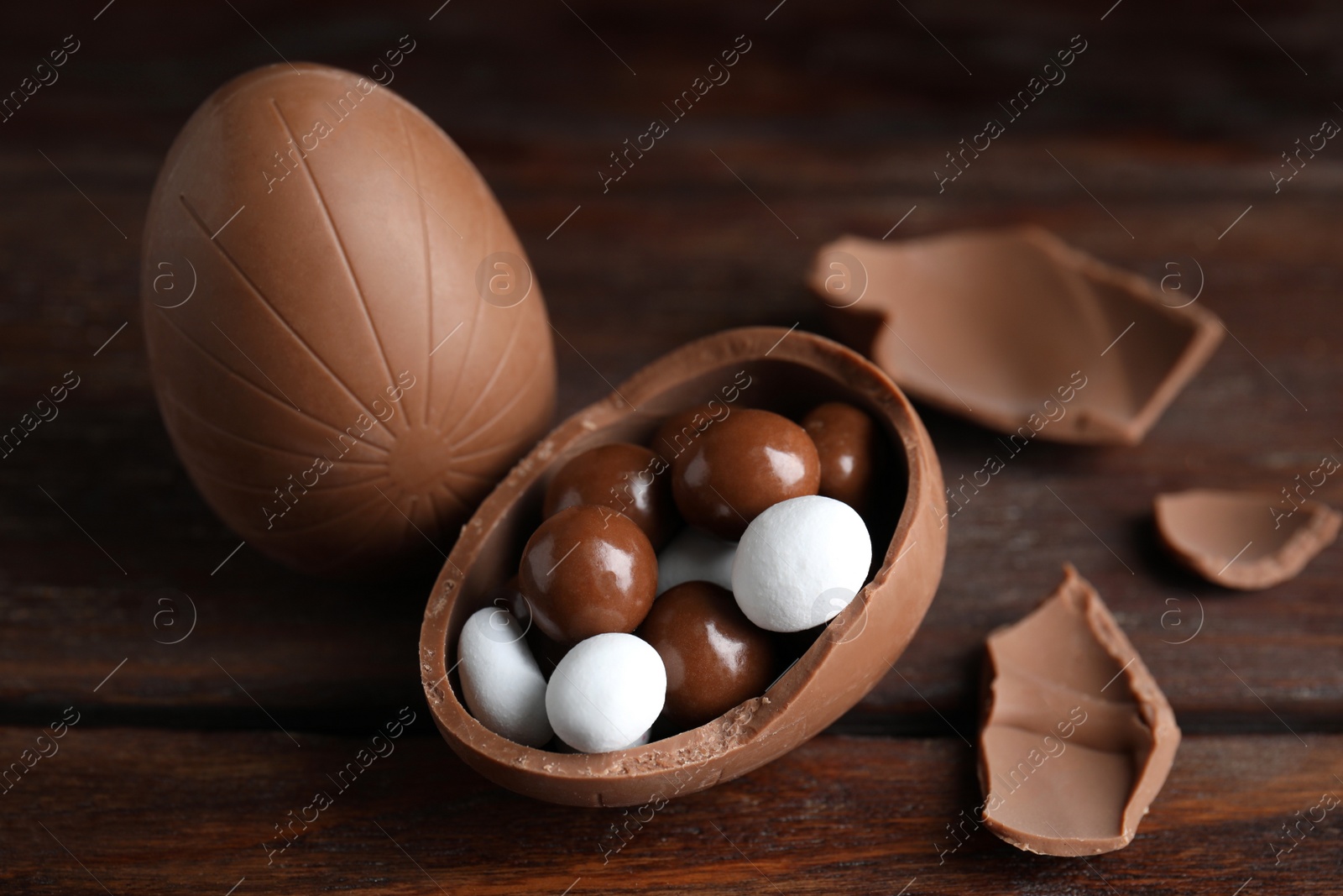 Photo of Whole and broken chocolate eggs with candies on wooden table